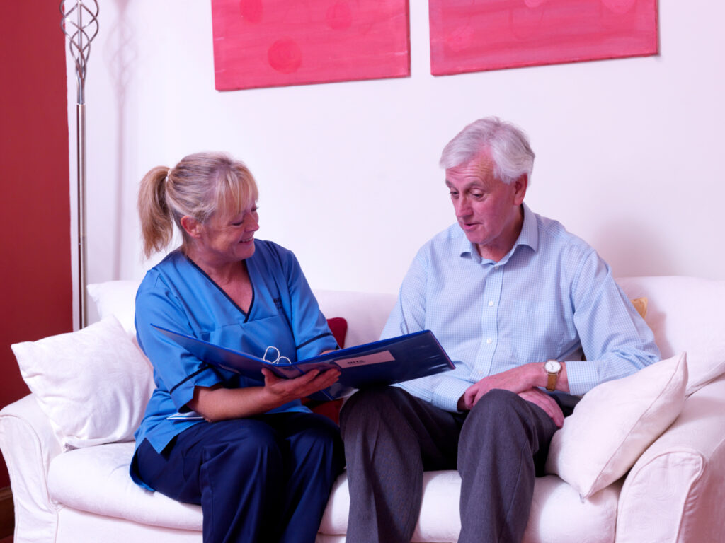 Patient and cancer nurse specialist holding a folder discussing whilst seated on sofa